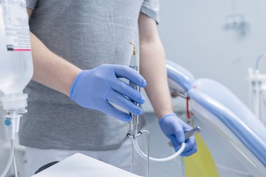 Parlak bir diş kliniğinde profesyonel temizlik sırasında ultrasonik pullu sulayıcıyla eldivenli dişçiyi kapat..