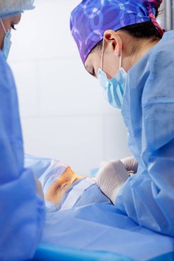 Bir oküloplastik cerrahın modern bir ameliyathanede steril perdelerin altında üst göz kapağını tedavi etmesi gibi..