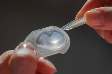 Aplikatör cımbızla tutulan yumuşak kontak lenslerin makro görünümü, steril günlük tek kullanımlık göz bakımı ve görüş düzeltmesi kavramı.