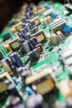 Parlak atölye ışığı altında kondansatör transformatörleri ve diğer güç bileşenleriyle yeşil elektronik devre kartının kapatılması