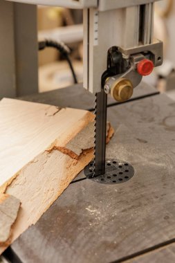 Dikey bant testeresi, kereste işleme ve güvenliğin sembolü tozlu ahşap atölyesinde ağaç kabuğu kenarlı çiğ tahta kesiyor.