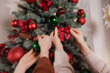 Noel ağacını kırmızı kurdeleler ve yeşil mücevherlerle dekore eden iki kişinin samimi bir ev içi şenliği..