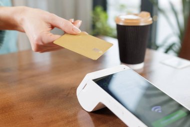 Banka kartını NFC POS terminalinin üzerinde, ahşap kafe masasında, parasız, teknoloji konseptiyle kapat.