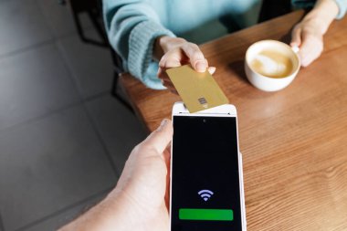 Akıllı telefon POS terminalindeki NFC banka kartının ahşap masada parasız kafe hesabı için dinlenmesi genel görünümü