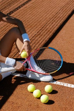 Tenisçinin yaz antrenmanı sırasında raket ve toplarla kil sahada dinlenme spor konseptini kapat.