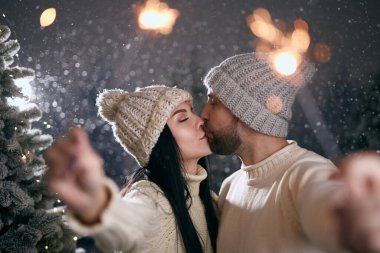 Beyaz kazaklı adam ve kız karlı bir ormanda maytap, kış ve noel konsepti