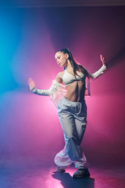 Gece kulübü ve dans promosyonu için mavi ve pembe ışıklı neon caz funk hip hop tarzı poz veren genç bir kadının tam boy portresi