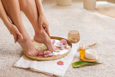 Ayaklarını taç yapraklarıyla ıslatan bir kadın pedikür için aloe vera yağı ve krem kullanıyor.