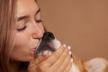 Genç bir kadının Corgi 'nin köpek ağızlığını öptüğü yakın plan. Sıcak ev hayatı sahnesinde şefkat, yakınlık ve arkadaşlığı ifade ediyor.