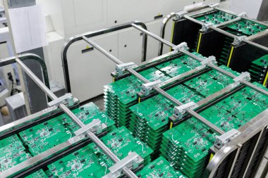 Modern otomatik elektronik üretim tesisinin içindeki metal raflara sıkıştırılmış yeşil baskılı devre kartları.