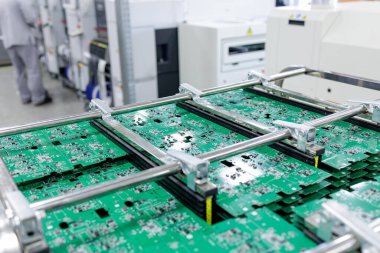 Çağdaş elektronik üretim tesisinin içinde metal raflara sıkıştırılmış yeşil devre kartları.