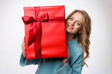 Gülümseyen kadın, beyaz arka planda kurdeleli kırmızı hediye kutusunun arkasından bakıyor, ekommerce afişi için ideal ya da web sitelerinde ve sosyal medyada tatil promosyonu için.