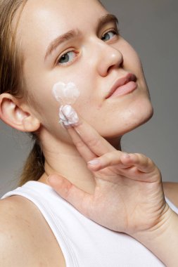 Sivilceye yüz nemlendirici uygulayan genç bir kadının stüdyo yakın çekimi. Cilt bakımı web sitesi afişi, kozmetik reklamcılığı veya sağlık blog içeriği için uygundur.