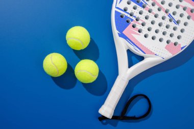 Padel tenis raketi ve toplar mavi arka planda düzgünce yerleştirildi. Reklam afişleri, spor web siteleri ve tanıtım amaçlı görsel içerik için ideal.