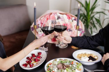 Mum ışığında, buket ve gurme tabaklar eşliğinde kadeh tokuşturan bir çift. Konukseverlik, flört ve pazarlama kampanyaları için ideal..