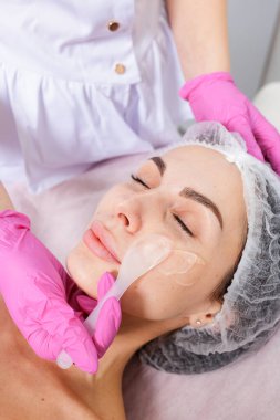 Kozmetik uzmanı, klinikte yüz tedavisi sırasında spatula kullanarak cilt maskesi takıyor. Güzellik, sağlık, dermatoloji ve kaplıca hizmeti için ideal..