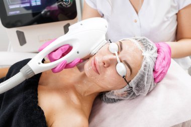 Kozmetik uzmanı, ışık cihazı kullanarak kadın müşterilere IPL fotorejuvenation prosedürü uyguluyor. Dermatoloji, estetik tıp ve gelişmiş cilt bakım hizmeti için ideal..