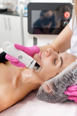 Kozmetik uzmanı kadın müşteriye deri temizleme cihazı kullanarak ultrasonik iyon temizleme yapıyor. Dermatoloji, estetik cilt bakımı ve profesyonel güzellik servisi tanıtımı için ideal..