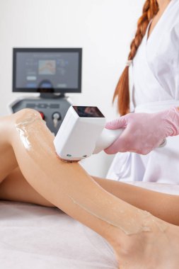 Kozmetik uzmanı, profesyonel aletle müşteri bacaklarında lazer tüyü çıkarıyor. Dermatoloji klinikleri, güzellik salonları ve kozmetik tedavi reklamları için uygundur..