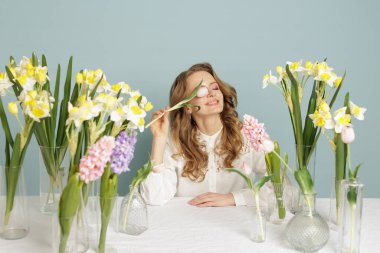 Stüdyoda bahar çiçekleriyle çevrili lale tutan gülümseyen bir çiçekçi kadın. Çiçekçilik, mevsimlik reklamcılık ve markalaşma kampanyaları için ideal..