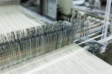 Kumaş üretimi sırasında dokuma tezgahlarından geçen ipliklerin ayrıntılı görünümü, tekstil üretimi reklamcılığı, endüstriyel markalaşma ve teknoloji içeriği için ideal.