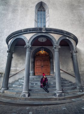 İsviçre 'deki eski gotik binanın merdivenlerinde oturan kadın.