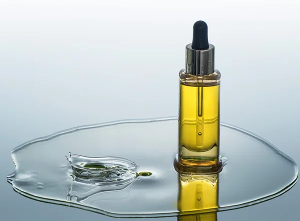 Butelka kosmetycznych oleju stoi na tle wody z splash — Zdjęcie stockowe