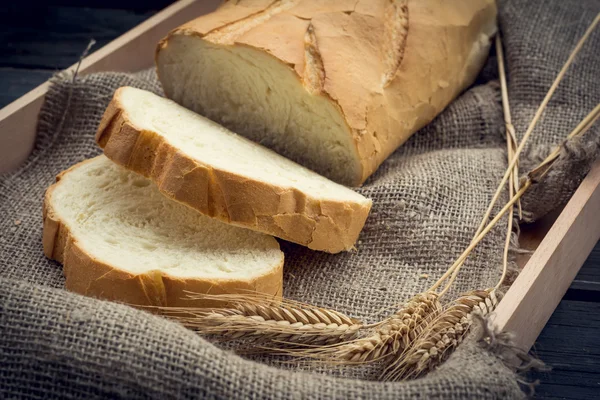 Pão branco fresco com espiguetas de trigo na bandeja de madeira — Fotografia de Stock