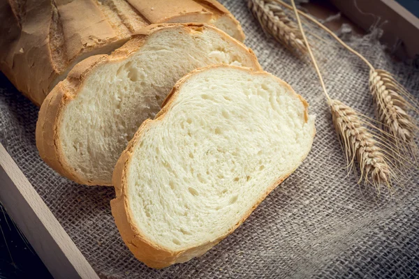 Pão branco fresco fatiado e trigo no fundo de linho — Fotografia de Stock