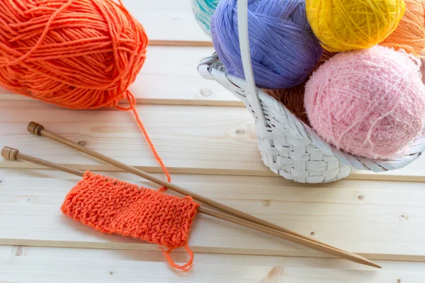 Incomplete breien project, houten naalden en witte mand met kleurrijke ballen van garen op achtergrond — Stockfoto
