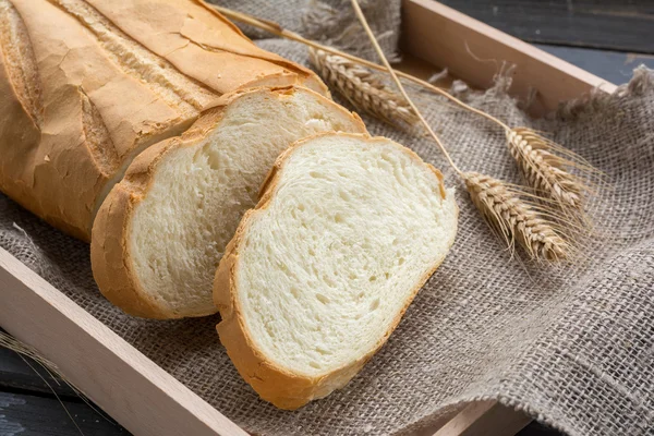 Нарезанная буханка белого хлеба и колоски пшеницы на мешковине — стоковое фото