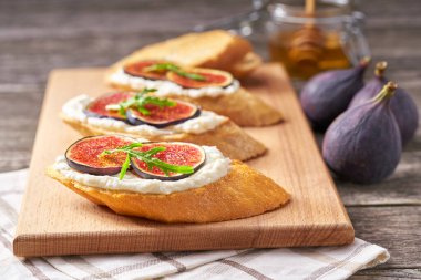 Krem peynirli sandviç, incir ve bal küçük bir kesim tahtasında servis edilir..