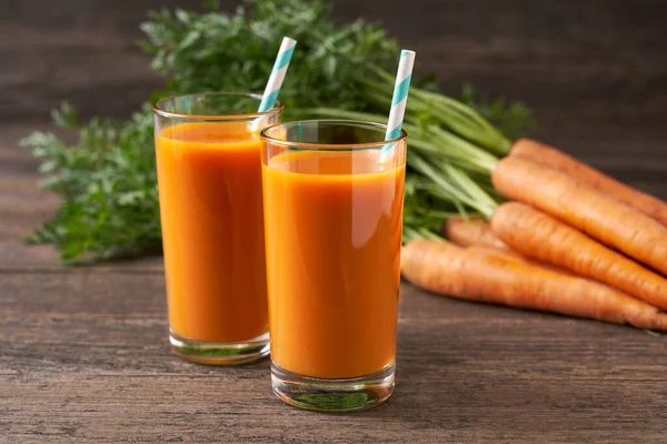 Glasses of carrot juice with vegetables on a rustic wooden table. Fresh carrot and juice (smoothies).