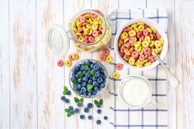 Renkli mısır halkaları ve açık mutfak masasında yaban mersini olan çocuklar için hızlı bir kahvaltı. Sağlıklı mısır gevreği meyveli kahvaltı için sütle meyveli döngüler oluşturur.