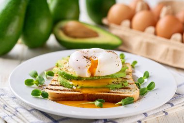 Avokadolu sandviç ve beyaz bir masada haşlanmış yumurta, seçici bir odak noktası. Dilimlenmiş avokadoyla tost ve sağlıklı kahvaltı veya atıştırmalık için bir fincan kahveyle yumurta..