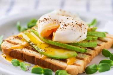 Avokadolu sandviç ve beyaz bir masada haşlanmış yumurta, seçici bir odak noktası. Dilimlenmiş avokadoyla tost ve sağlıklı kahvaltı veya atıştırmalık için bir fincan kahveyle yumurta..