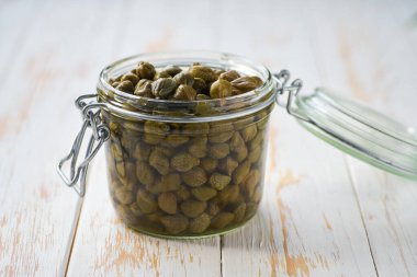 Beyaz ahşap bir masada cam kavanozda turşu tomurcukları, seçici bir odak noktası..