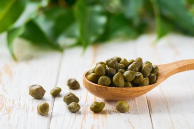 Tahta bir kaşıkta terbiye edilmiş kapari beyaz tahta bir masada, seçici bir odak.