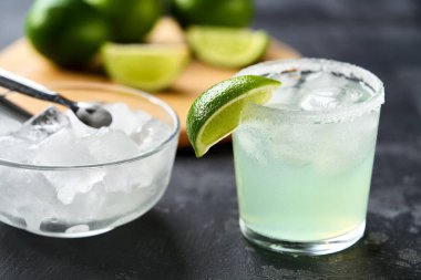 Limonlu ve buzlu Margarita kokteyli. Kesme tahtasındaki limon dilimlerinin yanında süzgeç camı..