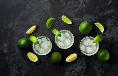 Siyah bir masada limon parçalarıyla margarita kokteyllerinin üst görüntüsü, metin için boşluk kopyala.