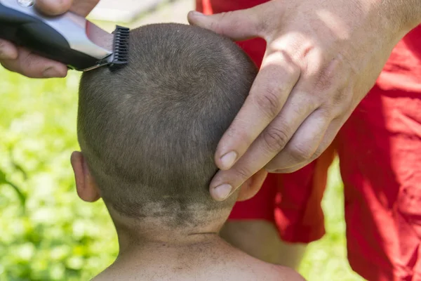 hand holds an electric hair clipper and cuts the boys long hair, barbershop at home, parent cuts hair while hairdressers are closed, stay home concept. toned