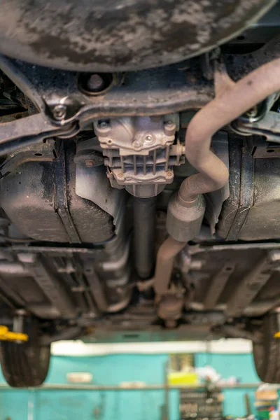 Car lifted in automobile service for fixing, worker repairs detail, telephoto. Car maintenance shop. Lifted chassis car for repairing under the car in garage shop. vertical photo