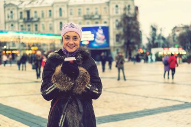 Şehirde kahve fincanı olan güzel genç bir kadın. Kışlık kıyafetlerle sokakta kahve içen güzel bir kadın. Kadın kış pazarında sıcak bir şeyler içiyor. ses tonlu.