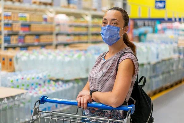 Alarmed female wears medical mask against coronavirus while shopping in supermarket or store- health, safety and pandemic concept. Girl shopaholic in mall. vertical photo. toned.