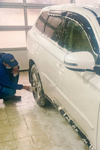 Washing a white car. Man worker washing windshield with sponge on a car wash. Manual car wash in car wash shop service. toned. vertical photo.