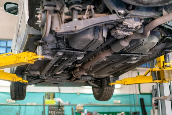 Car lifted in automobile service for fixing, worker repairs detail, telephoto. Car maintenance shop. Lifted chassis car for repairing under the car in garage shop.