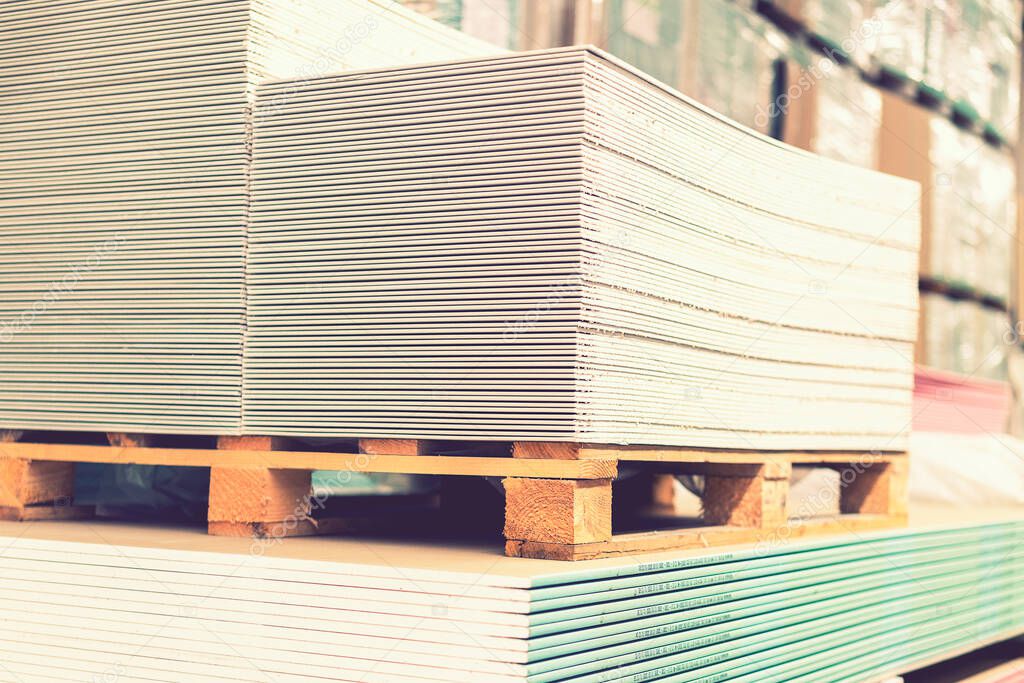 Pallet with Drywall sheets plasterboard in the building warehouse store. Stacking of white gypsum panels, drywall or plasterboard. Gypsum plasterboard in the pack. toned.