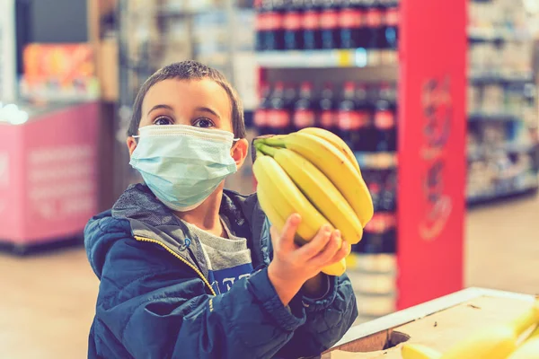 Cerrahi maske takan bir çocuk Coronavirus salgınında marketten meyve alıyor. Süpermarketteki küçük çocuk tıbbi maske takıyor. Coronavirus karantinası. Ton gibi. seçili odak — Stok fotoğraf
