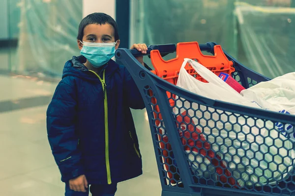 Çocuk mağazada koruyucu maske takıyor. Coronavirüs salgını sırasında alışveriş zamanı. Tıbbi maskeli bir çocuk. Virüs salgını sırasında çocuklarla alışveriş yapmak. Süpermarkette maskeli bir çocuk. ses tonlu — Stok fotoğraf