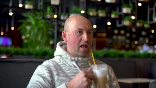 Trendig attraktiv man dricker kaffe i caféet. Snygg man dricker kaffe på caféet. Frukost- och kaffepaus. En skallig kille på ett kafé dricker cappuccino — Stockvideo